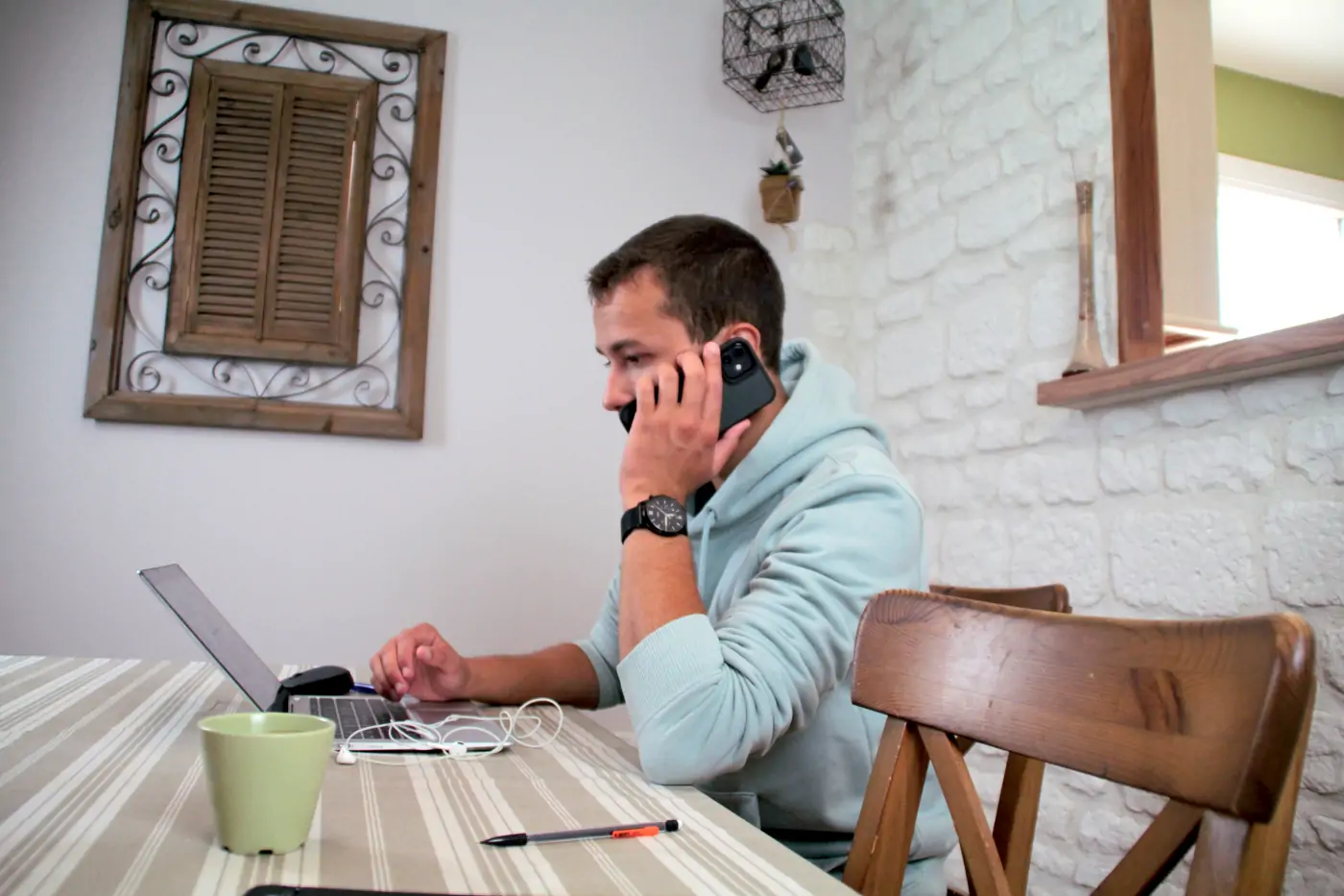 Notre webmaster assis à une table derrière son ordinateur portable en plein appel téléphonique.