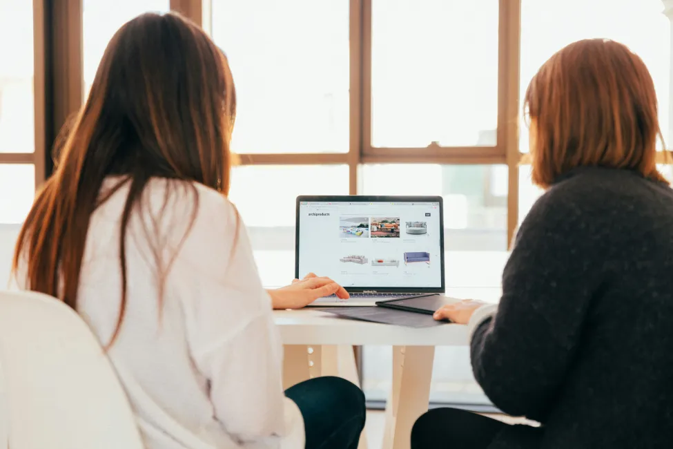 Deux personnes de dos regardant un site web sur un ordinateur portable posé sur une table.